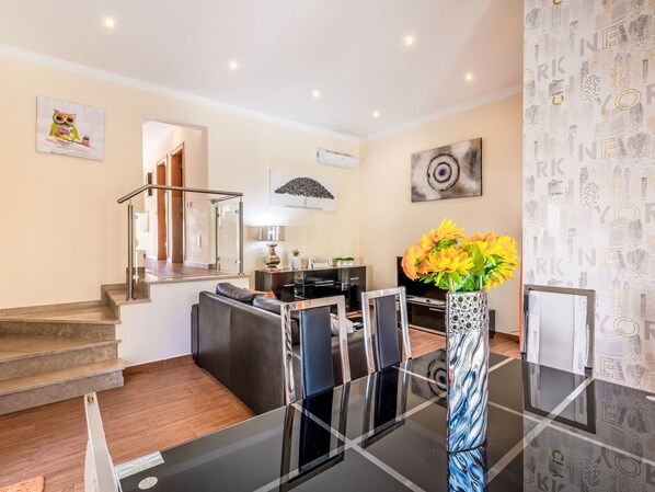 A modern living room with a glass-top dining table, a sofa, and a staircase leading to another level.
