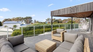 An outdoor patio with wicker furniture, a hanging chair, and a view of trees and buildings. - Luxury Beachside Entertainer With Heated Pool (St Leonards)