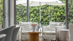 A modern indoor seating area with white furniture, a round wooden table, and a vase of flowers. - Luxury Beachside Entertainer With Heated Pool (St Leonards)