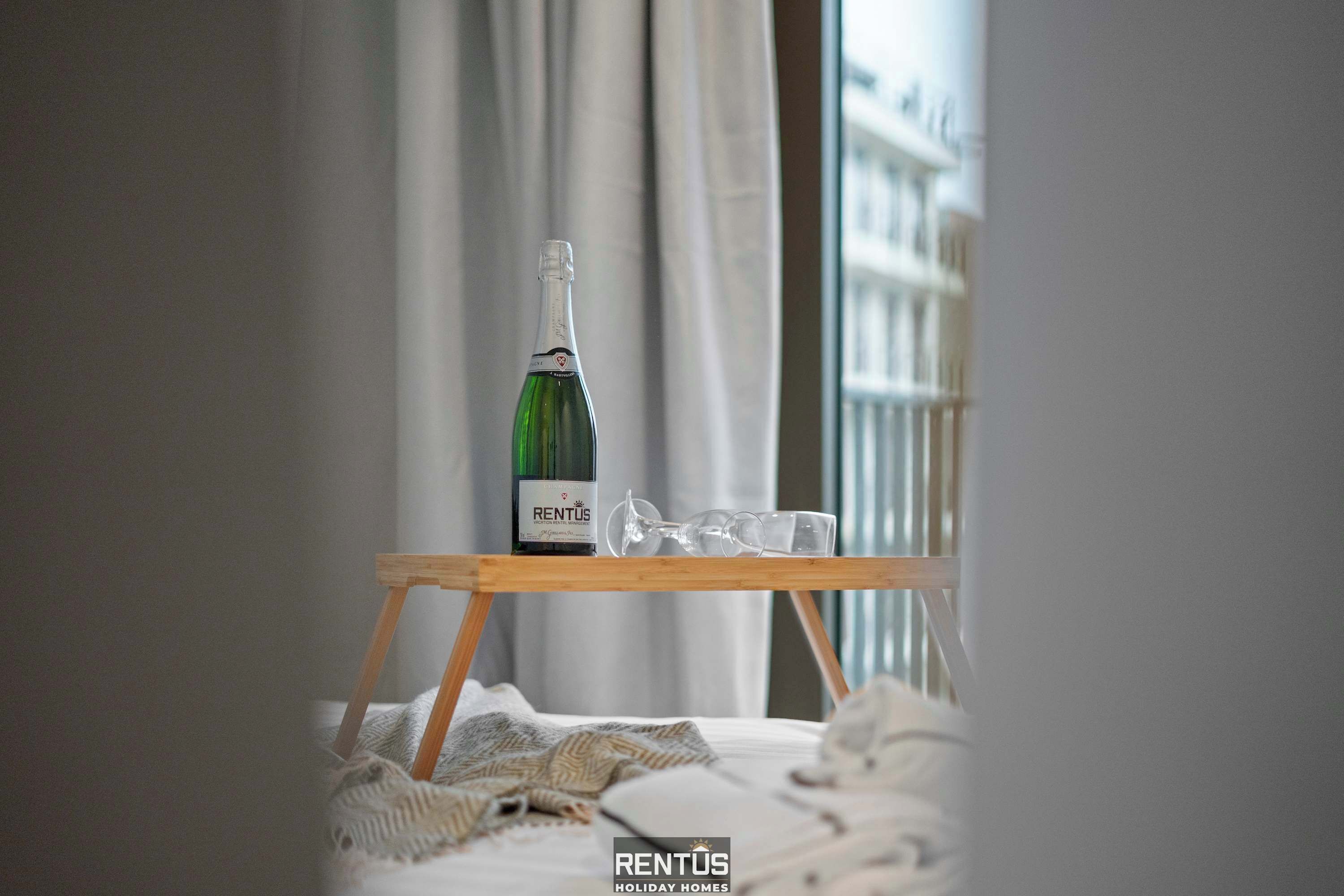 Eine Flasche RENTUS Wein steht auf einem Holztisch in einem Zimmer mit Blick auf Gebäude durch ein Fenster.