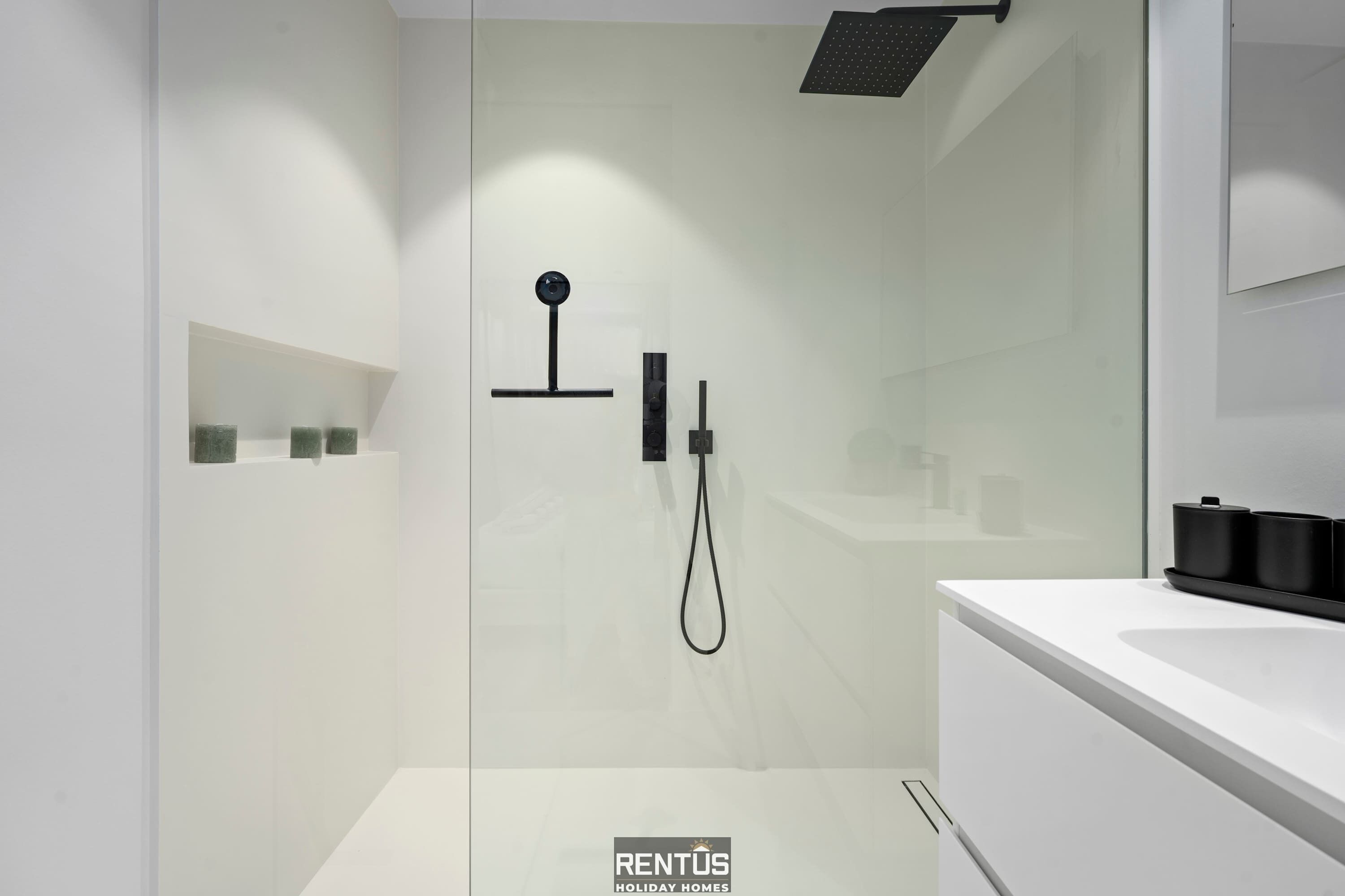 Un bagno moderno con cabina doccia in vetro, un lavandino bianco e un portasciugamani nero.
