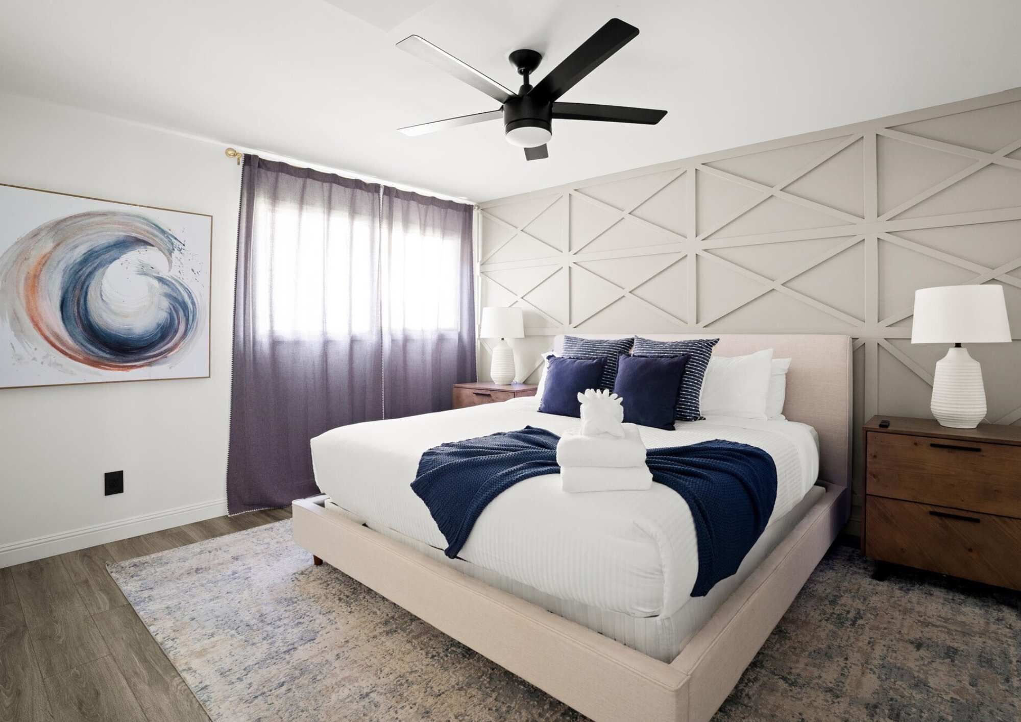 A modern bedroom with a bed, a ceiling fan, a nightstand, and a wall-mounted lamp.