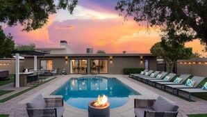 A modern outdoor pool area with lounge chairs, a fire pit, and a patio with a dining setup. - Backyard Arcade | Mini Golf, Pool & Hot Tub (Scottsdale)