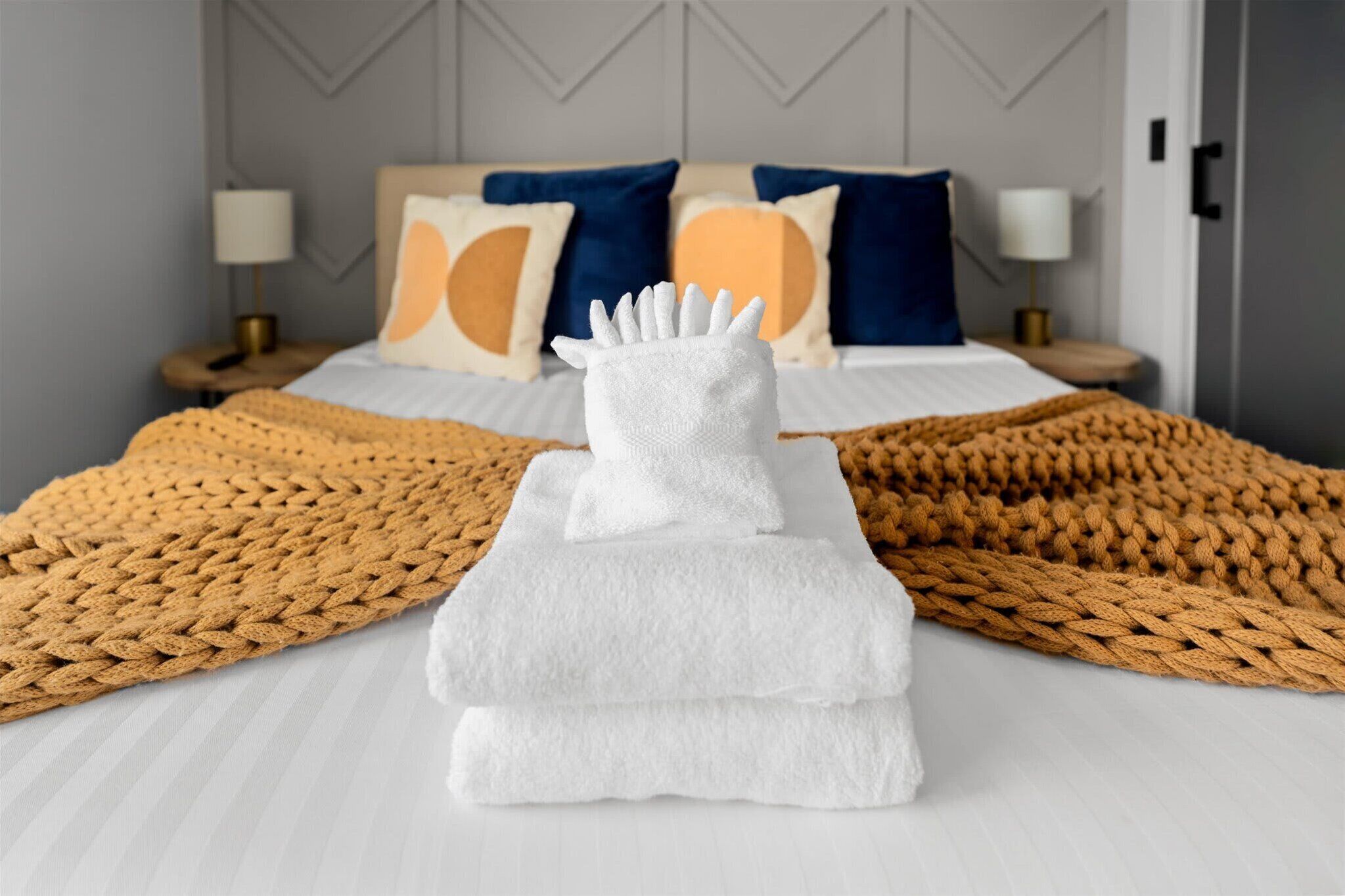 A neatly made bed with a white towel and a brown knitted blanket.