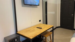 A room with a wooden table, a TV mounted on the wall, a safe, and a door.