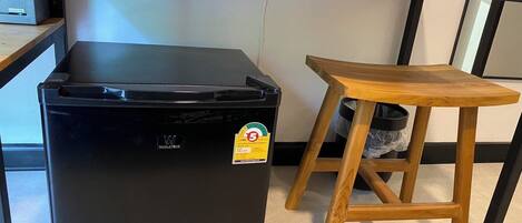 Un refrigerador negro compacto con una etiqueta de reciclaje, un taburete de madera y una encimera de cocina.