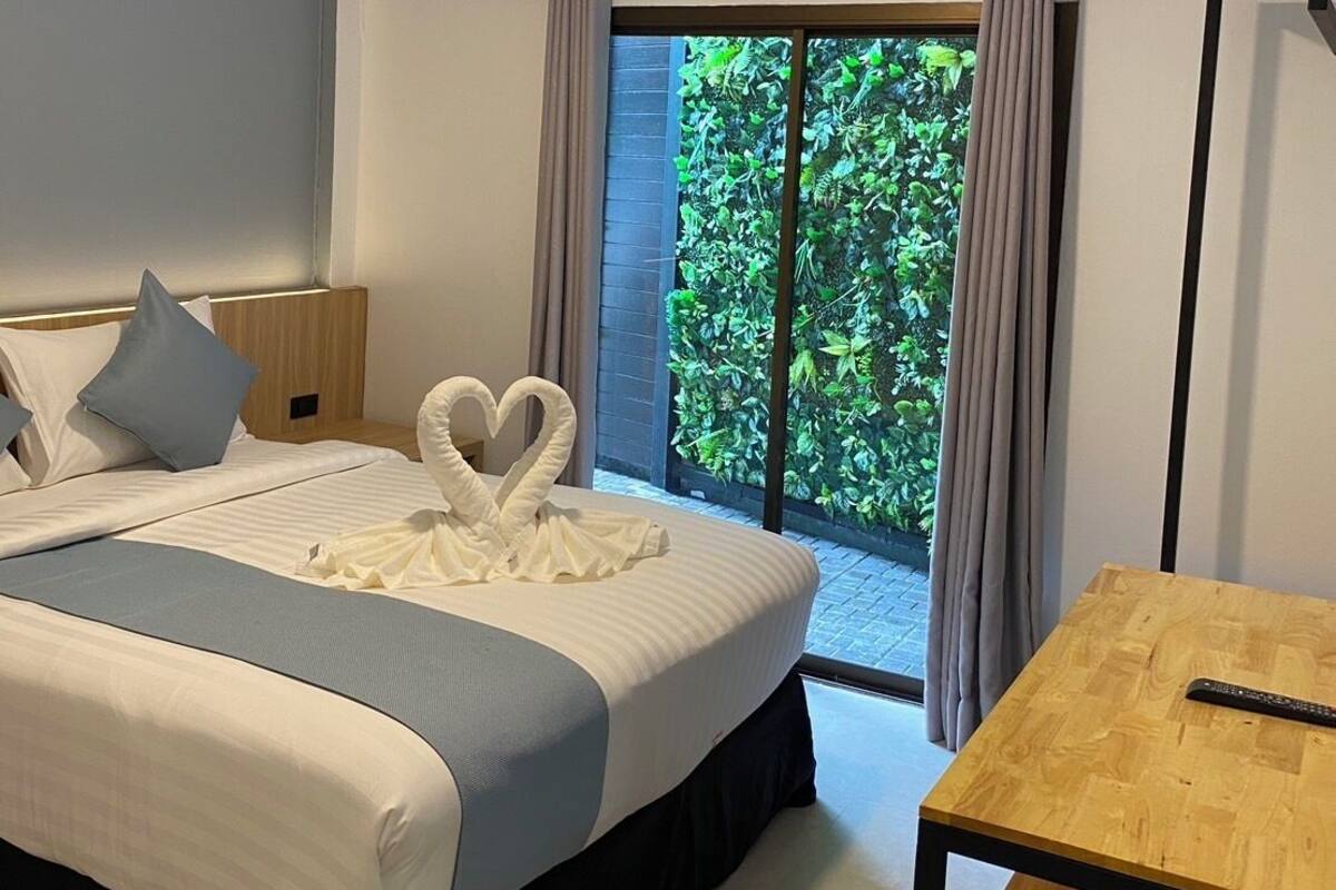 Une chambre d’hôtel avec un lit, une table en bois et une vue sur la verdure, visible à travers une porte coulissante.