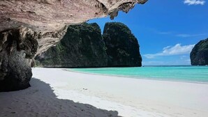 A beach with white sand and clear turquoise water, surrounded by large rock formations.