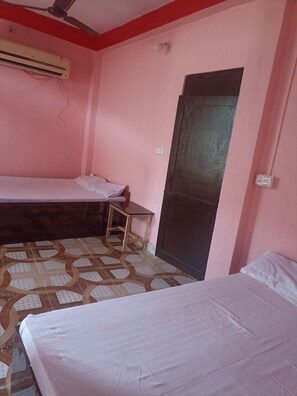 A room with two beds, a small table, an air conditioning unit, and a door. - Laliguras Hotel and Lodge  (Manthali)