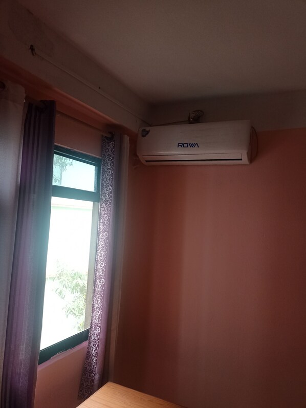An air conditioning unit mounted on a wall above a window with patterned curtains.