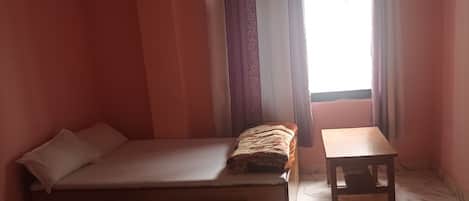 A room with a bed, a small table, and a window with curtains.
