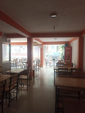 A restaurant with wooden tables and chairs, a Coca-Cola refrigerator, and a view of the street outside.