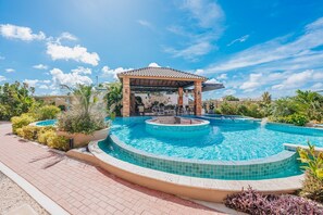 A swimming pool with a sunken hot tub, surrounded by a covered seating area and lush landscaping. - 9BR House Pool Gym 7-Min Walk Palm Beach Porta Al Sole #2,3&4 by Bocobay (Noord)