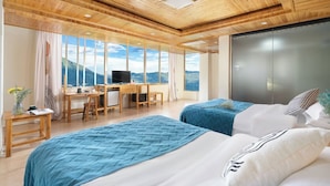 Una camera d'albergo moderna con soffitti in legno, ampie finestre che offrono vista sulle montagne, due letti, una scrivania e un televisore.