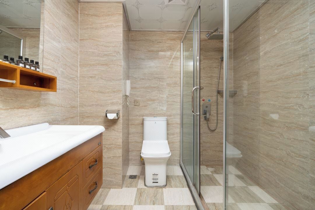 A modern bathroom with a glass shower enclosure, a white toilet, and a wooden vanity with a white countertop.