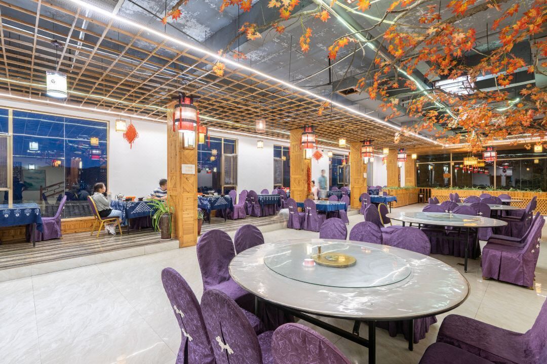Un amplio comedor interior con mesas redondas y sillas moradas, que presenta un diseño moderno de techo con adornos colgantes.
