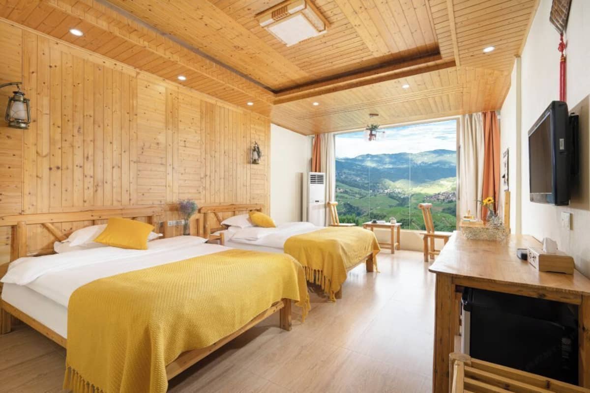 A wooden cabin-style room with two beds, a TV, and a view of a mountainous landscape.