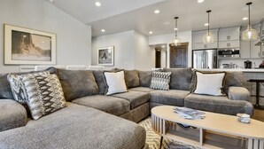 Una sala moderna con un sofá modular, una mesa de centro y una cocina al fondo.