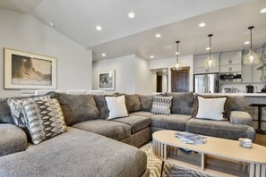 A modern living room with a sectional sofa, a coffee table, and a kitchen in the background.
