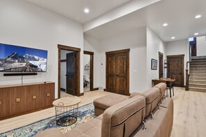 Un salon spacieux doté d’un grand téléviseur à écran plat, d’un ensemble de canapés, d’une table basse et d’un tapis à motifs.