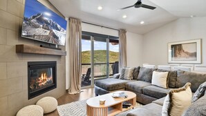 Una sala de estar moderna con chimenea, un televisor de pantalla plana grande, un conjunto de sofás y un balcón con vistas.