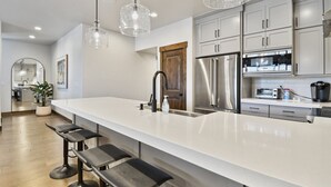 Una cocina moderna con una isla grande, electrodomésticos de acero inoxidable, iluminación colgante y una puerta de madera.