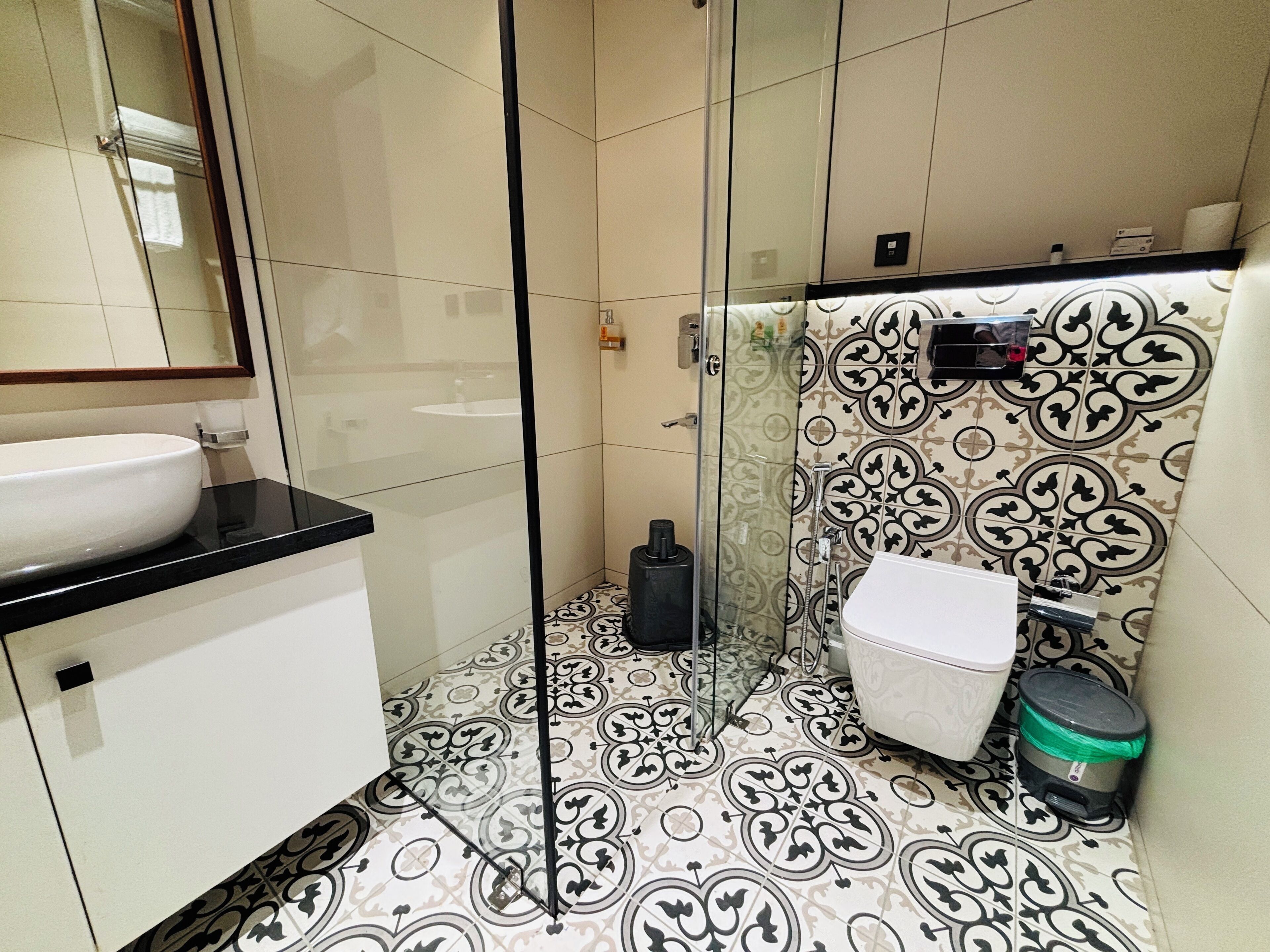 Un bagno con doccia vetrata, lavandino bianco e piastrelle decorate.