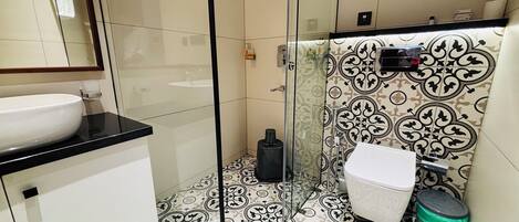 A bathroom with a glass-enclosed shower, a white sink, and patterned floor tiles.