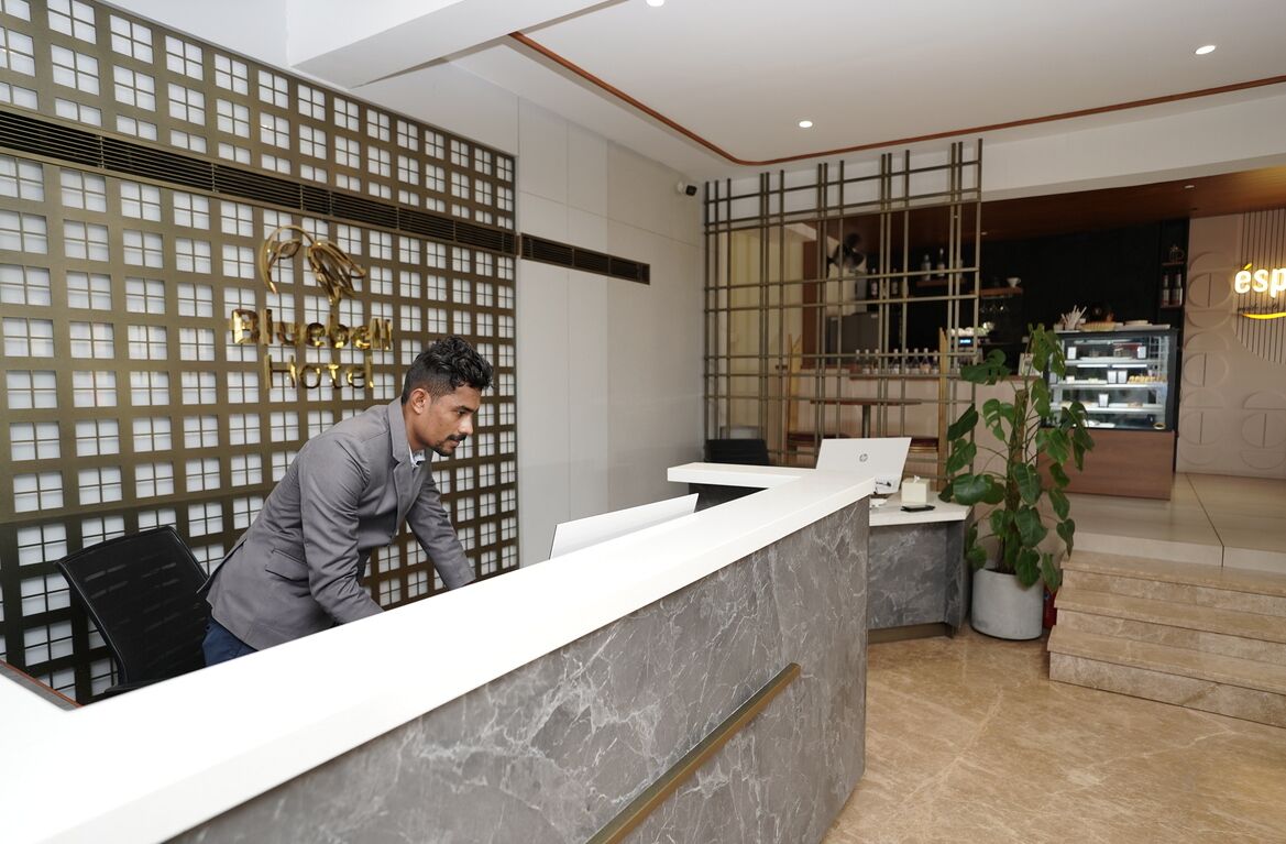 A hotel reception area with a modern design, featuring a reception desk, a decorative wall with a grid pattern, and a visible sign for the hotel.