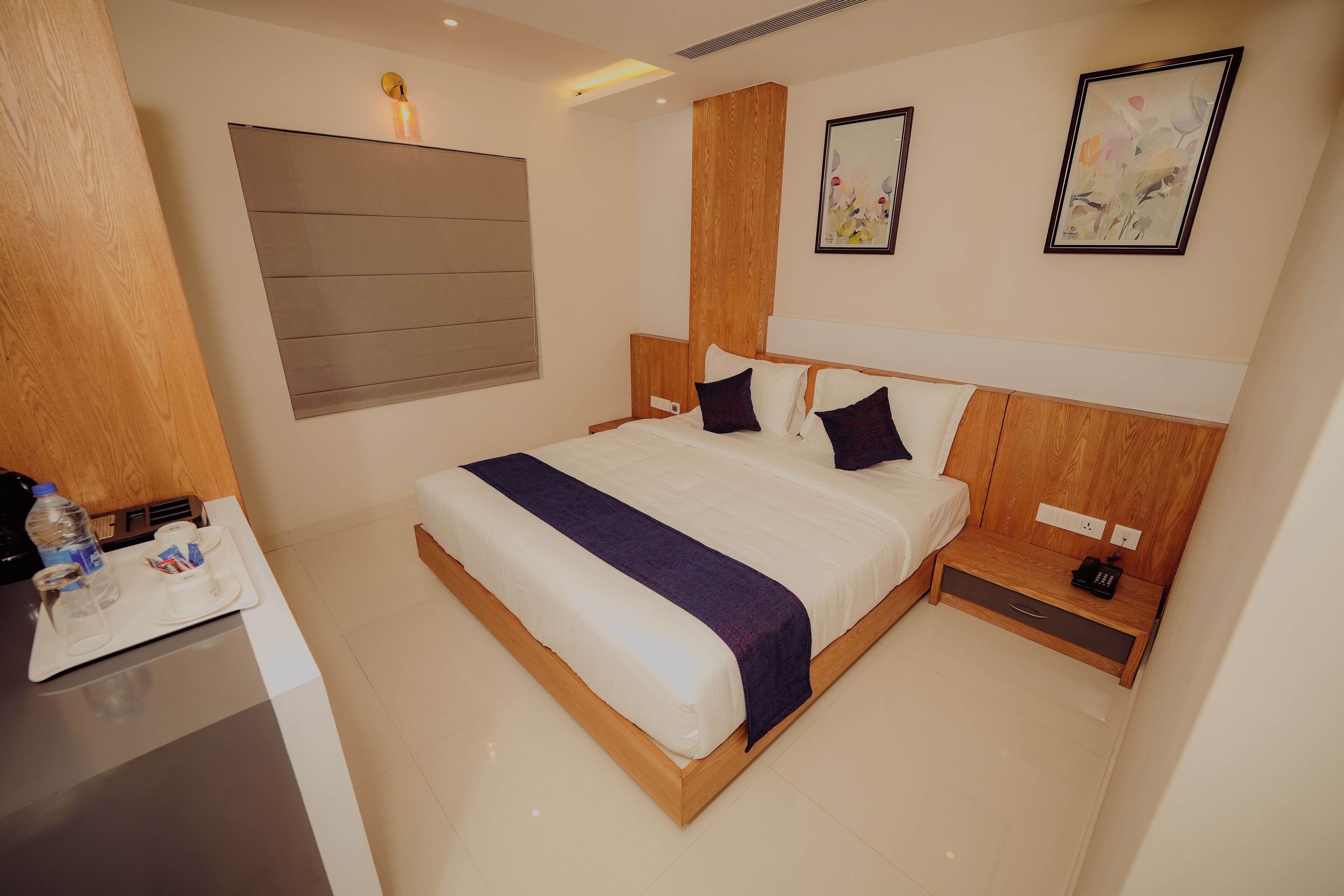 A modern hotel room with a large bed, wooden headboard, bedside tables, and artwork on the walls.