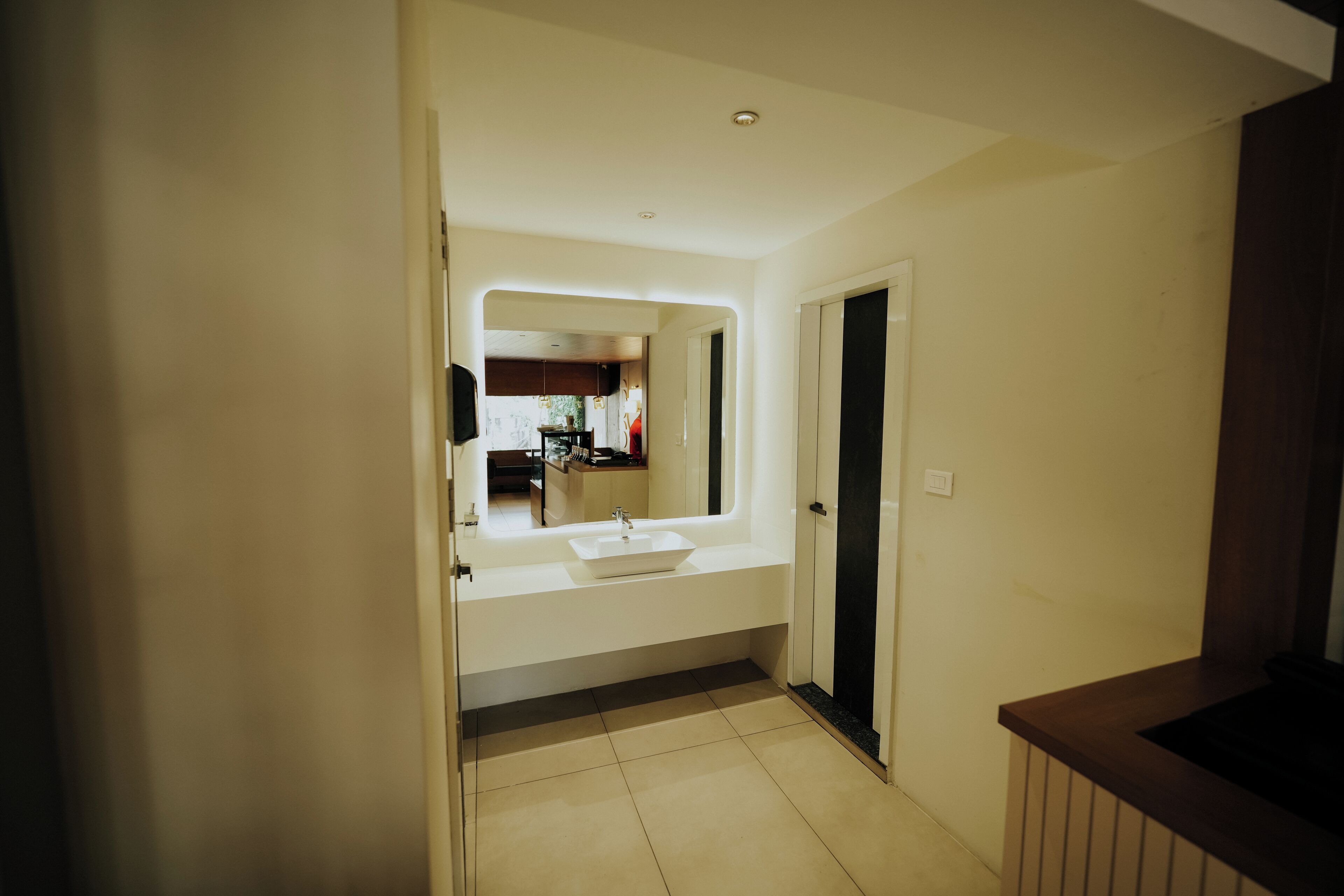 A modern bathroom with a large sink, a mirror, and a door leading to another room.