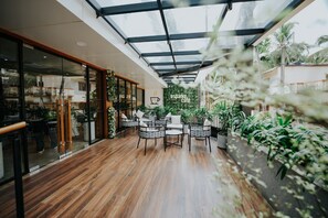 A modern cafe with wooden flooring, glass walls, and indoor plants. - Hotel Blubell (Kozhikode)