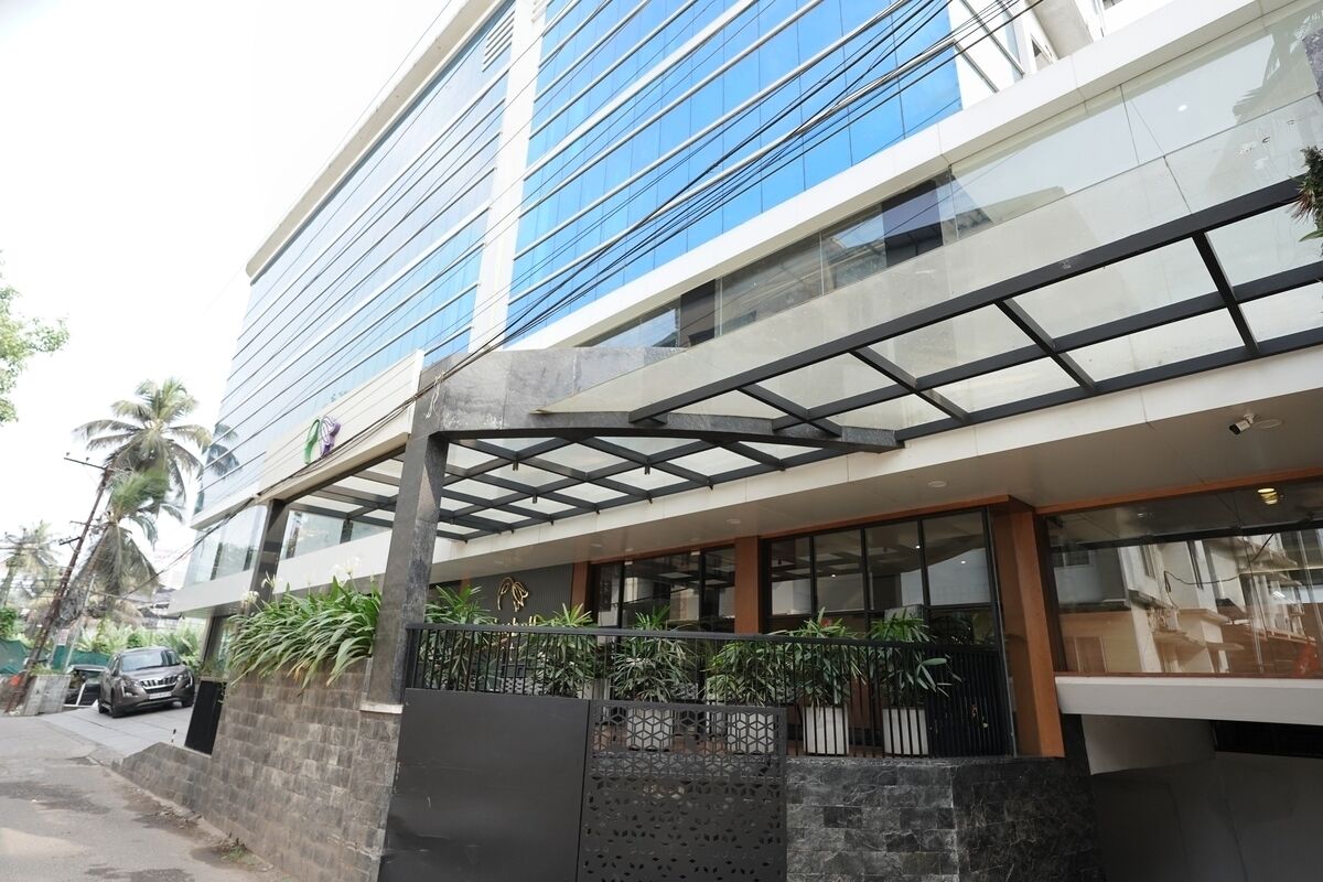 Un edificio moderno con fachada de vidrio, zona de estar al aire libre techada y una pared de piedra con plantas en macetas.