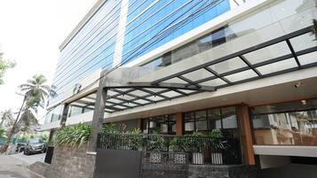 Un edificio moderno con fachada de vidrio, zona de estar al aire libre techada y una pared de piedra con plantas en macetas.