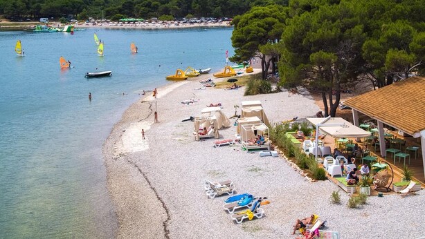 A beach with clear waters, beach umbrellas, and a small building with outdoor seating.
