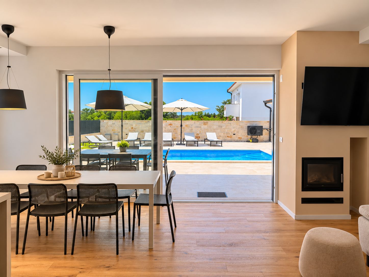 Uma sala de estar moderna com vista para a piscina, uma área de jantar com cadeiras e mesa, e uma lareira.