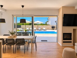 Ein modernes Wohnzimmer mit Blick auf einen Pool, einer Essecke mit Stühlen und einem Tisch sowie einem Kamin.