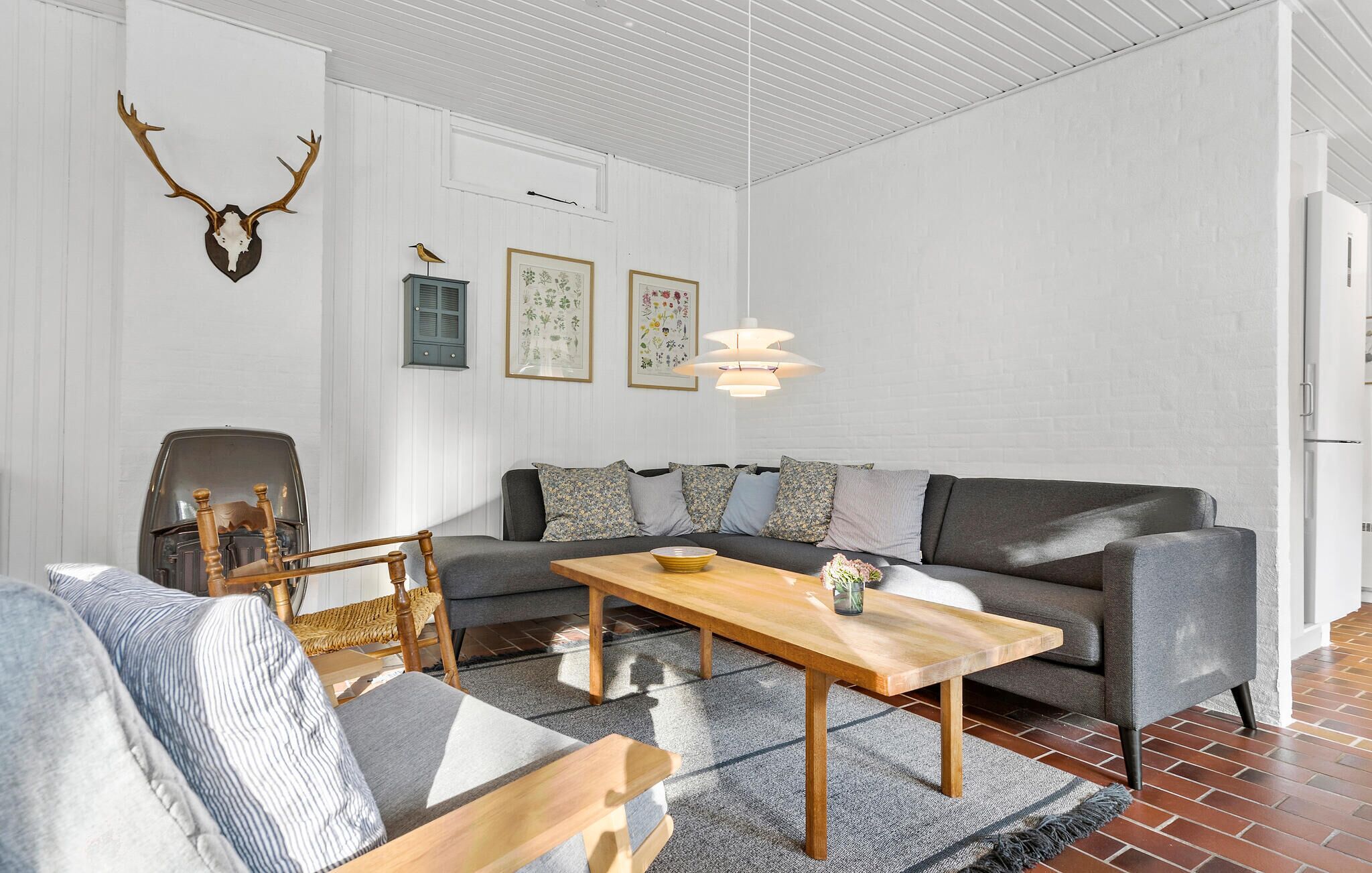 En moderne stue med en sofa, et træsofabord og en lænestol. Der er et vægmonteret dådyrskranium og indrammede botaniske tryk.