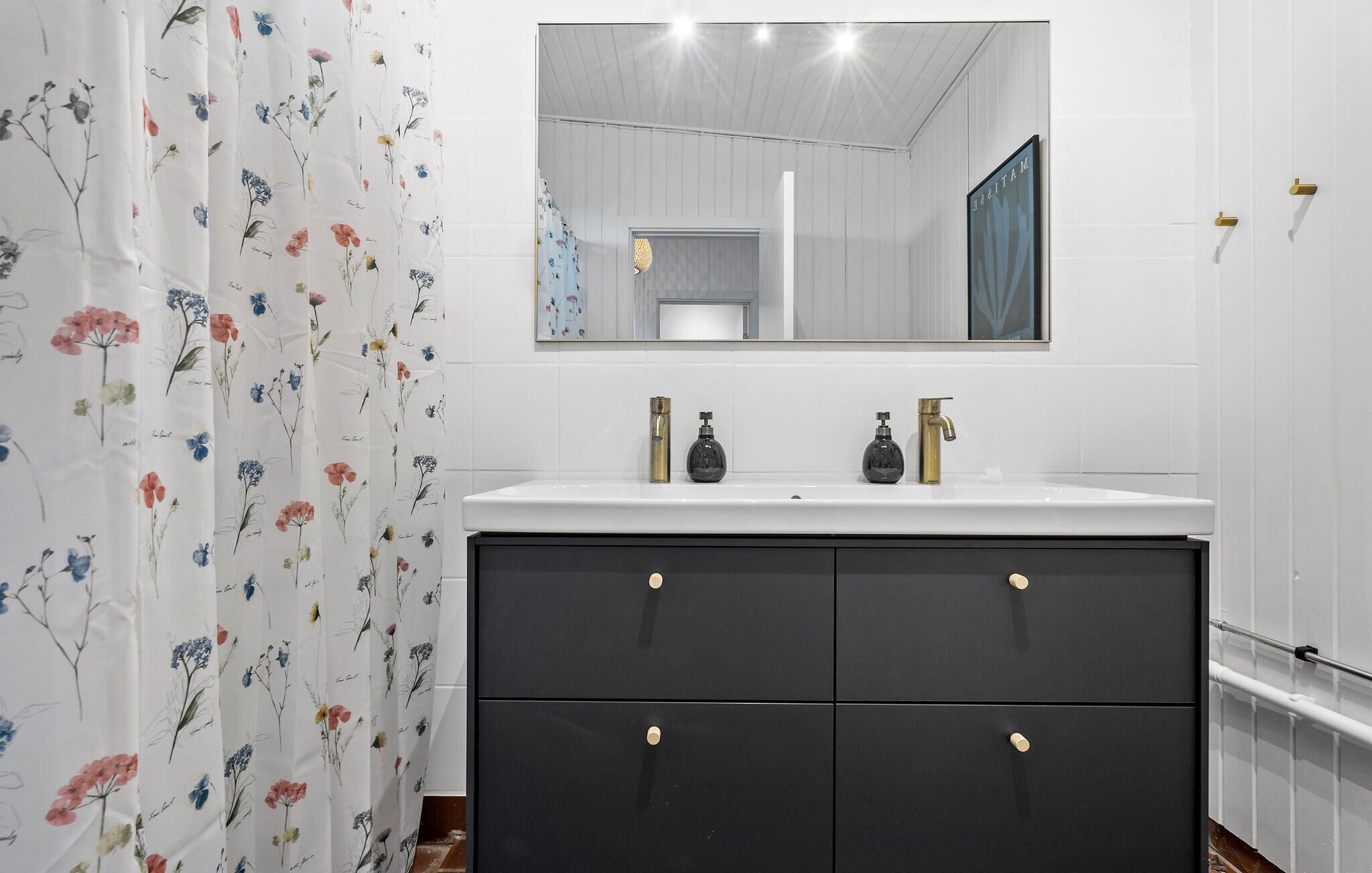 A bathroom with a white sink, two faucets, and a black vanity with drawers.