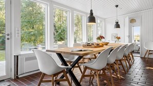 A spacious dining area with a long wooden table, white chairs, and pendant lighting.