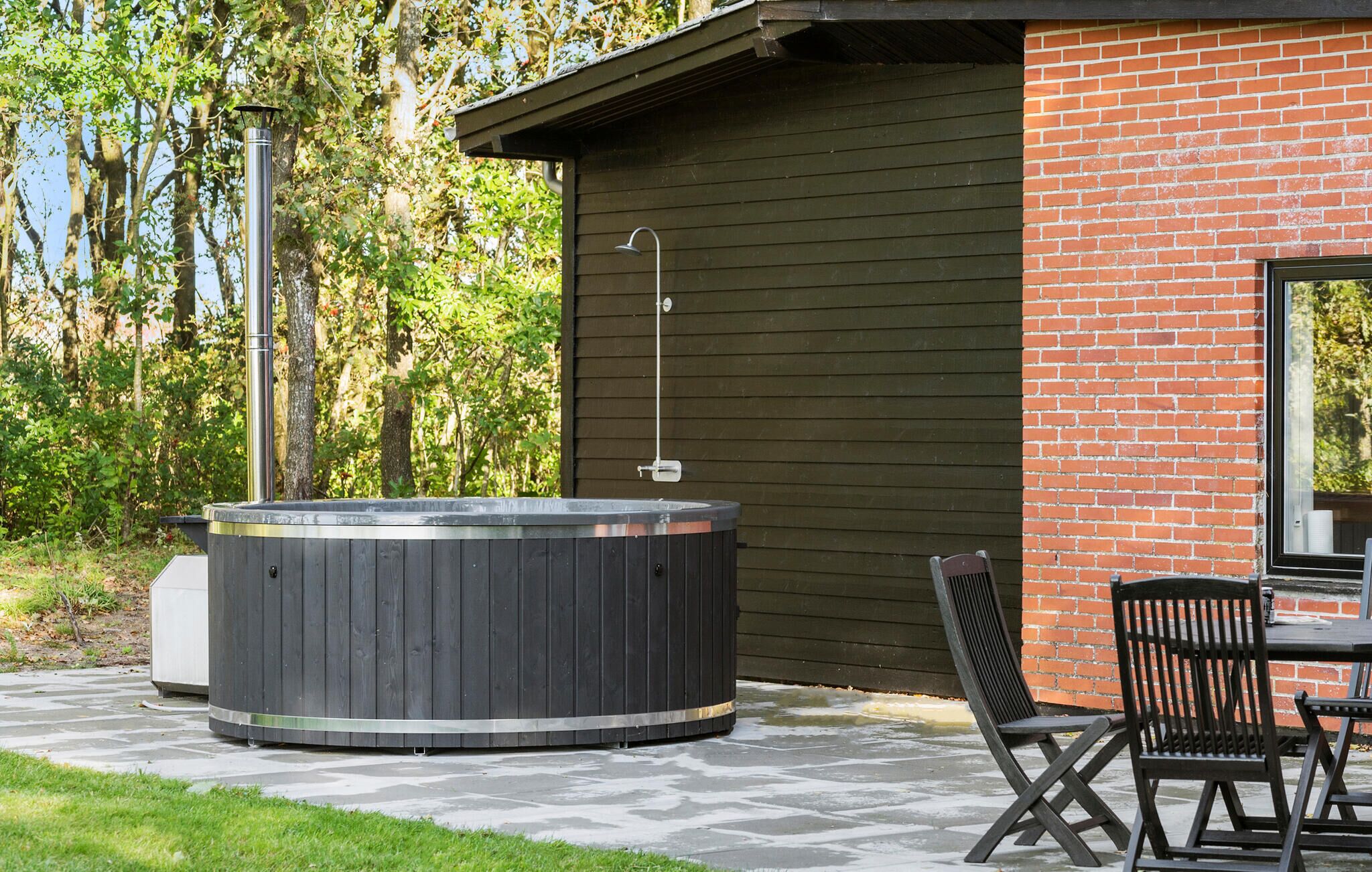 A hot tub in a garden area with a brick wall and wooden deck.