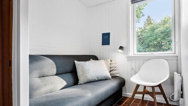 A modern living room with a grey sofa, a white chair, and a window with a view of trees.