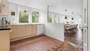 A modern kitchen with large windows, a dining area with a brick floor, and a white partition.
