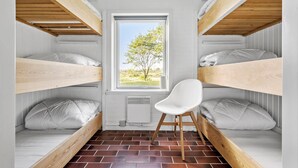 A room with two bunk beds, a white chair, and a window with a view of trees.
