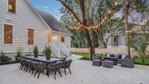 A house with a patio area featuring a dining table and chairs, a seating area with cushions, and string lights. - Private Pool + Fire Pit + Foosball | Short Walk to Beach | Southern Oasis (Isle Of Palms)