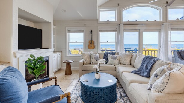 A living room with a sofa, a coffee table, and a TV mounted on the wall. - Beachfront w/ Pool, Hot Tub & Game Room, Sleeps 28 | Atlantic Watch by AvantStay (Kill Devil Hills)