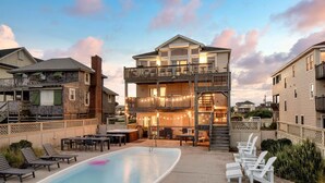 A two-story house with a balcony, a swimming pool, and outdoor seating. - Beachfront w/ Pool, Hot Tub & Game Room, Sleeps 28 | Atlantic Watch by AvantStay (Kill Devil Hills)