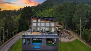 Una casa moderna con un amplio ventanal de vidrio, una terraza en la azotea y una piscina.