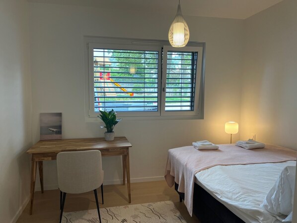 A bedroom with a bed, bedside table, lamp, desk, chair, window with blinds, and a potted plant. - Luxury lakeside home Geneva Lausanne (Rolle)