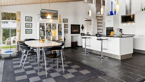 Una cocina moderna con una isla central, taburetes de bar y una zona de comedor con alfombra a cuadros.